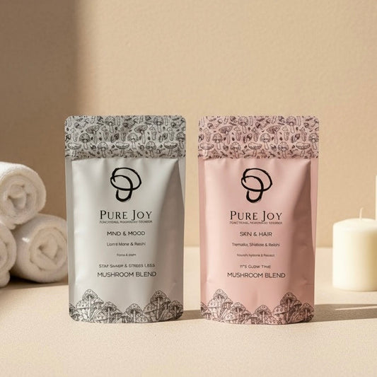 Two packages of Pure Joy mushroom blend on a light surface with towels and a candle in the background.