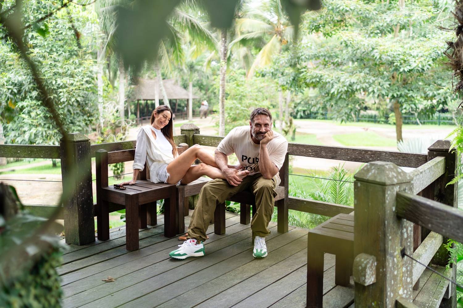 Two people relaxing on a wooden deck with a lush green tropical garden in the background